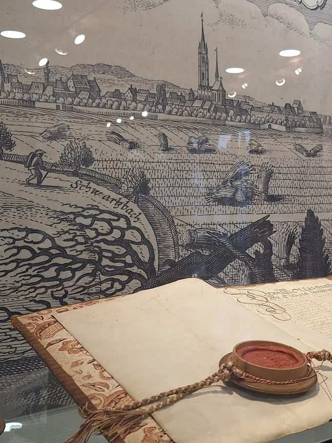 Historische Stadturkunde mit Siegel vor einer alten Stadtansicht von Groß-Gerau in der Vitrine.